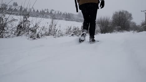 Primer-Plano-De-Bajo-Nivel-De-Pies-Masculinos-Caminando-Por-La-Nieve-Frente-A-Cabañas-De-Madera