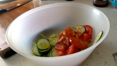 Pouring-olive-oil-on-sliced-mixed-vegetables-in-a-plastic-bowl