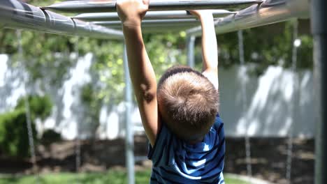Slow-Motion-shot-of-a-young-boy-playing-on-the-monkey-bars-on-a-playground-set-in-his-backyard