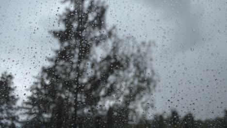 Regentropfen-Bewegen-Sich-Auf-Das-Fenster,-Während-Draußen-Ein-Regnerischer-Und-Windiger-Tag-Ist