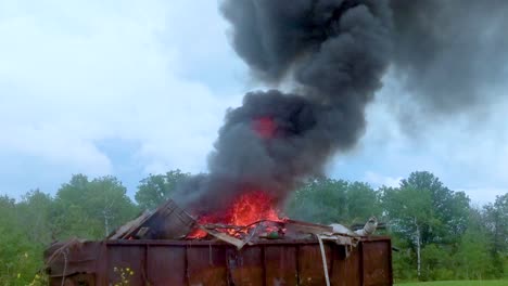 Thick-dark-smoke-billowing-from-a-burning-dumpster-full-of-garbage-on-rural-farmland