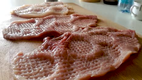 Seasoning-sliced-and-tenderized-pork-loins-on-a-chopping-board-with-coarse-sea-salt