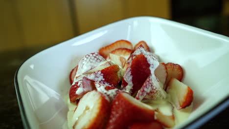 Thick-cream-is-slowly-dripping-over-cut-ripe-strawberries-in-a-bowl