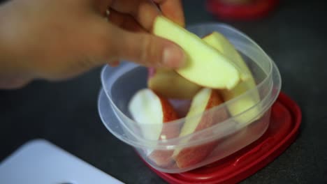 Slow-Motion-Shot-of-someone-putting-freshly-cut-apple-slices-into-a-small-Tupperware-container