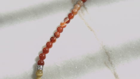 Sliding-shot-of-red-jasper-beads-in-a-prayer-mala-placed-on-a-white-marble-slab-shot-in-UHD-4K