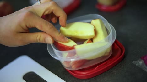 Slow-Motion-Shot-of-someone-putting-freshly-cut-apple-slices-into-a-small-Tupperware-container