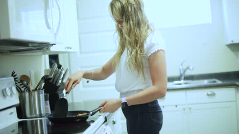 Handheld-slow-motion-shot-of-a-young-blonde-female-cooking-chicken-in-a-pan-over-a-stove