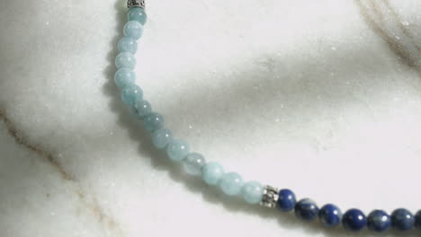 Dolly-macro-shot-of-blue-Celestite-beads-from-Tibetan-prayer-mala-placed-on-white-marble-shot-in-UHD