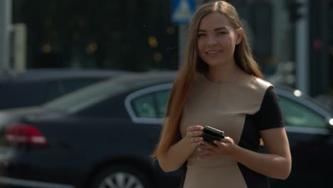 A-beautiful-young-woman-in-the-center-of-a-large-city-next-to-a-large-road-intersection-uses-a-smartphone