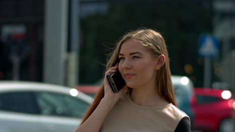 Beautiful-young-woman-in-the-center-of-a-large-city-next-to-a-large-road-intersection-uses-a-smartphone-to-talk-to-her-friend