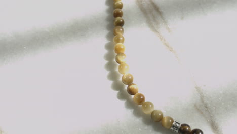 Gleitaufnahme-Von-Gelben-Tigerauge-Perlen-In-Einer-Gebets-Mala-Auf-Weißem-Marmor,-Aufnahme-In-Uhd