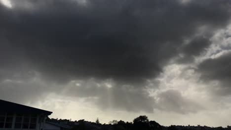 Dunkelgraue-Ominöse-Wolken-Mit-Sonnenstrahlen,-Die-über-Das-Stadtbild-Strahlen