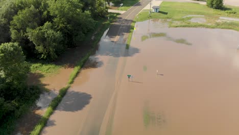 4k-rising-aerial-view-showing-flood-water-going-over-a-road-outside-of-a-small-town