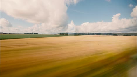 Fensterblick-Aus-Einem-Fahrenden-Zug-über-Gelbe-Und-Grüne-Felder-Mit-Geschwollenen-Weißen-Wolken-Am-Blauen-Himmel