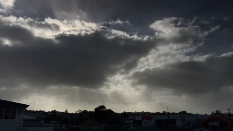 Dunkelgraue-Ominöse-Wolken-Mit-Ein-Paar-Sonnenstrahlen,-Die-Sich-über-Das-Graue-Stadtbild-Quälen