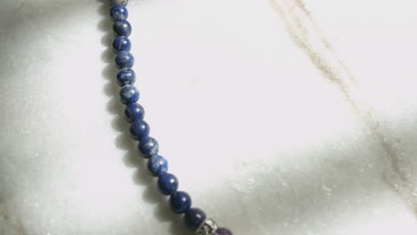 Macro-dolly-shot-of-blue-lapis-lazuli-beads-from-a-Tibetan-prayer-mala-resting-on-white-marble-slab-shot-in-UHD