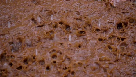 Slow-motion-shot-of-rain-drops-hitting-a-muddy-puddle-and-creating-interesting-patterns-with-the-splashes