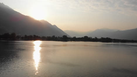 Stetiger-Schwenk-Bei-Sonnenaufgang-Am-Seeufer-Des-Lago-Maggiore-Mit-Den-Bergen-Im-Hintergrund,-Locarno,-Schweiz