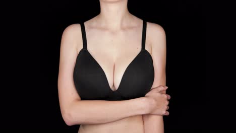 Woman-holds-left-arm-on-seamless-black-studio-background-wearing-a-black-bra