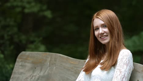 young,-red-haired-woman-sitting-on-a-wooden-bench-in-nature-smiling,-looking-into-the-lens-and-laughing