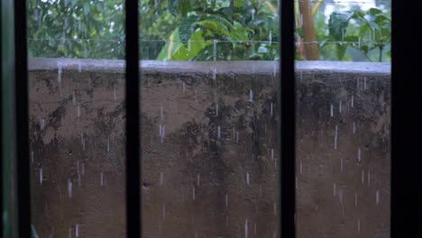 A-slow-motion-shot-from-within-a-locked-room-with-bars-looking-out-at-pouring-rain-in-a-walled-in-compound-with-barbed-wire
