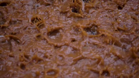 Close-up-slow-motion-shot-of-heavy-rain-falling-into-a-muddy-puddle-and-creating-splashes