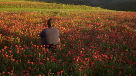 Man-sitting-in-a-field-of-beautiful-red-poppies-reflecting-on-life