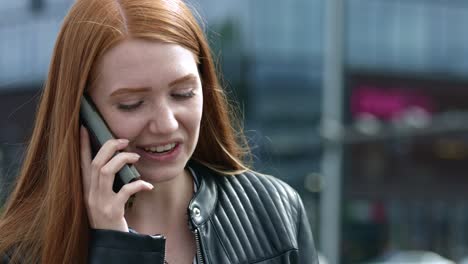 Close-up-of-young-red-haired-girl-with-freckles-on-the-phone-having-a-conversation-in-a-big-city-wearing-a-black-leather-jacket