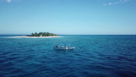 Dolly-Aéreo-Justo-Encima-Del-Hermoso-Océano-Turquesa-Se-Centra-En-Un-Barco-Flotante-Con-La-Playa-Tropical-Paradise-Southsea-Island-Como-Fondo-En-Fiji