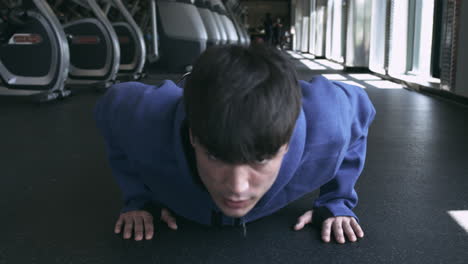 Straight-on-shot-of-millennial-male-doing-push-ups-on-the-gym-floor-stabilized-shot-in-UHD-4K