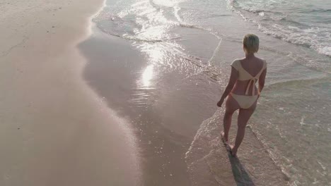 Una-Dama-En-Bikini,-Caminando-Sola-En-El-Agua-De-La-Playa-Para-Relajarse-Bajo-La-Luz-Del-Sol