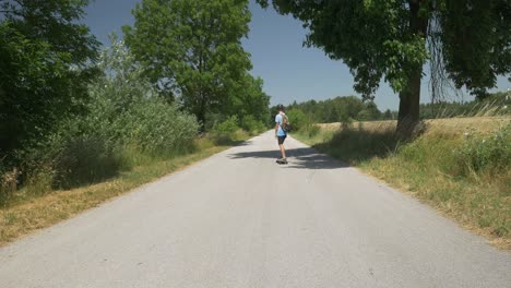 Driving-Electric-Skateboard-in-Helmet-On-Empty-Road-Below-The-Trees-Blue-Clear-Sky-Summer-4K