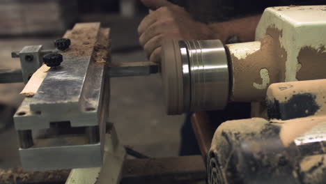 Sliding-shot-of-a-worker's-hands-carving-wood-on-a-factory-lathe
