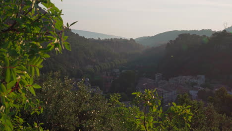 Camera-moving-up-from-between-the-trees-to-reveal-the-hidden-village-in-the-valley-in-the-Cote-d'Azur-region-in-France