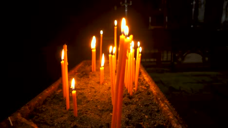 Long-red-candles-flicker-a-golden-yellow-as-the-camera-slowly-pans-around-them-at-a-shallow-depth-of-field