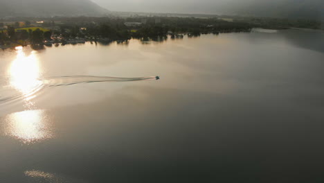Aerial-view-of-a-motorboat-boating-on-Lake-Maggiore-during-Sunrise---Aerial-pan-right-during-golden-hour