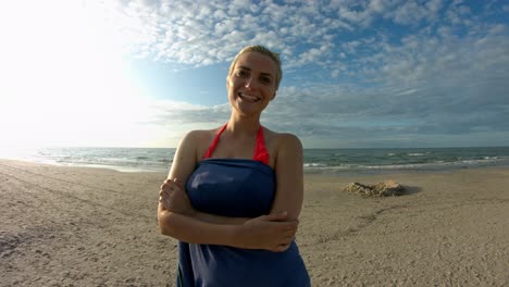 A-woman-with-short-blonde-hair-drying-off-after-taking-a-swim-at-the-beach,-smiling-and-laughing-at-the-camera