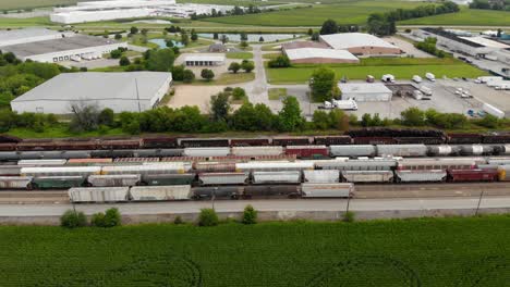 4k-aerial-footage-panning-left-to-right-of-multiple-trains-and-tracks-with-one-train-starting-to-move-and-a-small-town-in-the-background