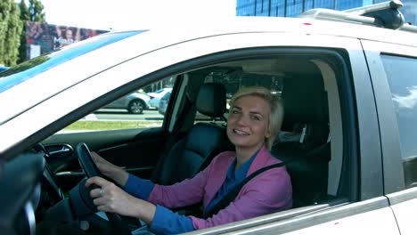 Beautiful-Blonde-Hair-Woman-Wearing-Pink-Long-Sleeve-Driving-The-Car-While-Smiling-On-The-Camera---Close-Up-Shot