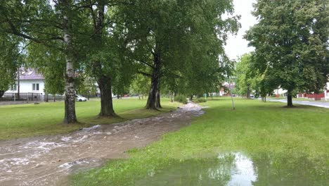 Flooded-river-running-through-a-park-in-Slovak-village,-Pan-shot