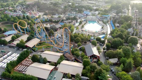 Aerial-descending-turning-shot-of-amusement-park-roller-coaster-rides-and-water-park-on-bright-sunny-summer-morning