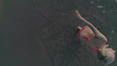 Aerial-high-angle-top-down-Shot-Of-young-woman-lying-on-the-beach-and-being-surprised-by-a-wave-of-the-ocean
