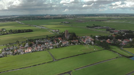 Nach-Oben-Geneigte-Antenne-Zeigt-Das-Dorf-Ransdorp-Mit-Seiner-Agrarischen-Umgebung-Und-Die-Stadt-Amsterdam-In-Den-Niederlanden-Im-Hintergrund-Vor-Einem-Blauen-Himmel-Mit-Wolken
