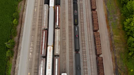 4k-aerial-view-of-multiple-trains-sitting-at-a-train-station-while-revealing-a-long-straight-railway-with-multiple-tracks-ahead-next-to-a-small-town