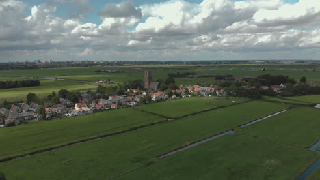 Aerial-tilt-down-showing-the-village-of-Ransdorp-with-its-agrarian-surroundings-and-the-city-of-Amsterdam-in-The-Netherlands-in-the-background-against-a-blue-sky-with-clouds
