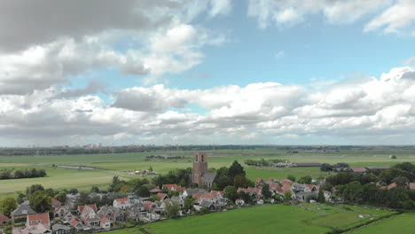 Aerial-tilt-up-showing-the-village-of-Ransdorp-with-its-agrarian-surroundings-and-the-city-of-Amsterdam-in-The-Netherlands-in-the-background-against-a-blue-sky-with-clouds