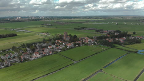Aerial-tilt-down-showing-the-village-of-Ransdorp-with-its-agrarian-surroundings-and-the-city-of-Amsterdam-in-The-Netherlands-in-the-background-against-a-blue-sky-with-clouds-passing-by