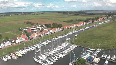 Aerial-steady-and-rotation-shot-following-the-movement-of-a-sailboat-in-the-marine-port-area-for-pleasure-boats-with-typical-houses-of-the-Dutch-village-of-Durgerdam-against-a-blue-sky-with-clouds