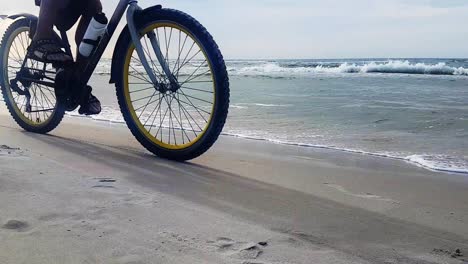 Hombre-Montando-Bicicleta-En-La-Playa-De-Arena-En-Un-Día-Nublado