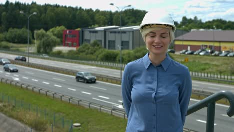 Mujer-En-El-Sitio-De-Construcción-Con-Un-Sombrero-Duro-De-Pie-Sobre-Una-Autopista-Con-Una-Gran-Sonrisa